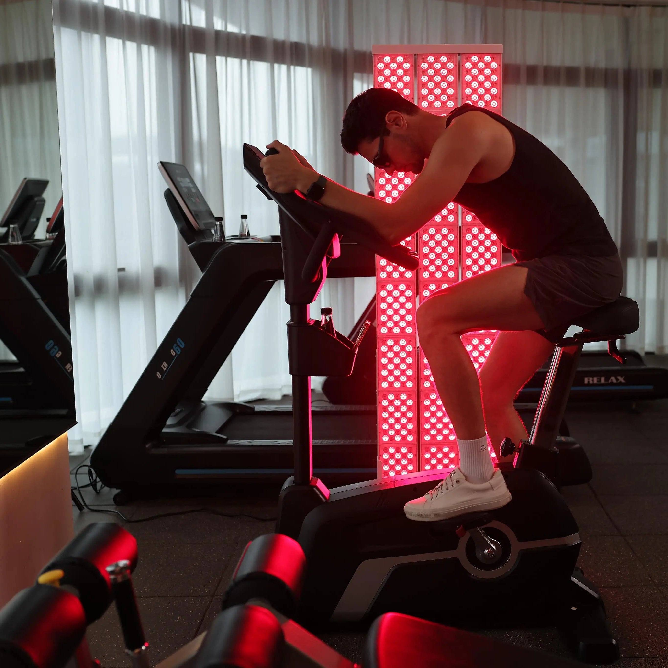Man using a red light therapy panel while cycling indoors for faster recovery and enhanced workout performance
