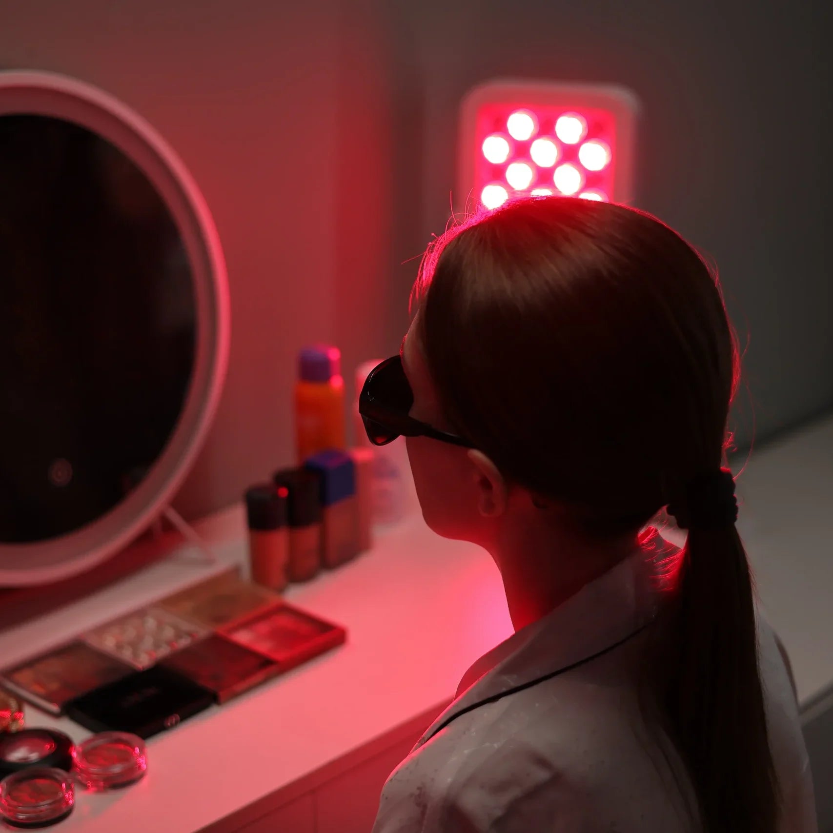 Woman wearing eye protection using a YouLumi red light therapy panel for facial skin care at her vanity