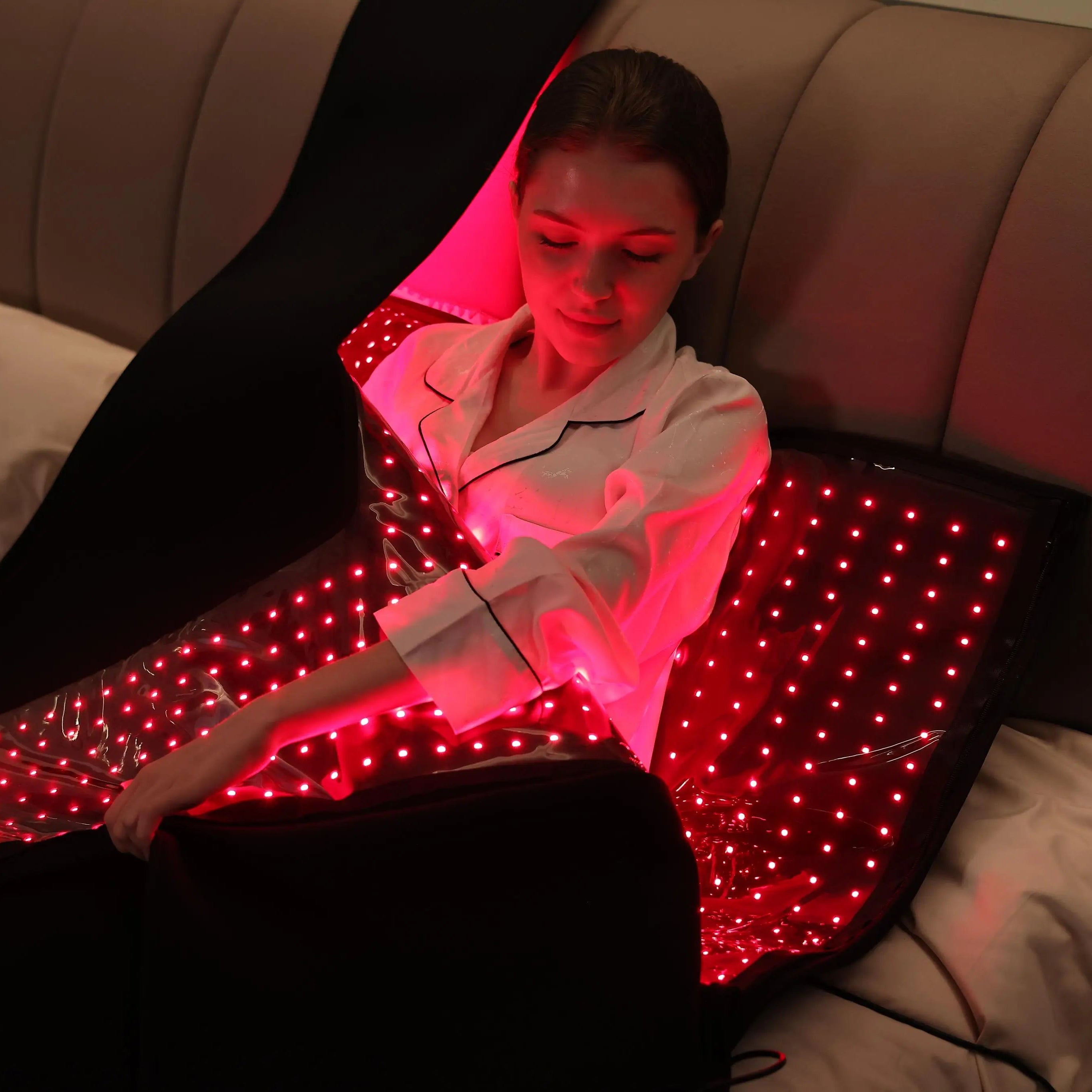 User relaxing on bed using the YouLumi red light therapy mat; flexible wrap design with bright red LEDs for full-body session.
