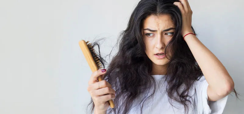 A person looking thoughtfully at hair on their brush, concerned about hair fall and seeking solutions