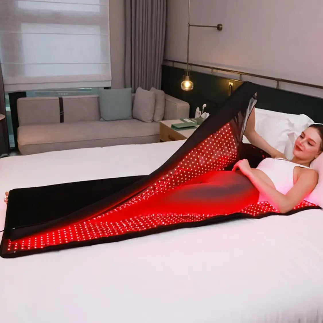 Woman relaxing inside a red light therapy blanket on a bed, demonstrating full-body recovery and wellness benefits at home
