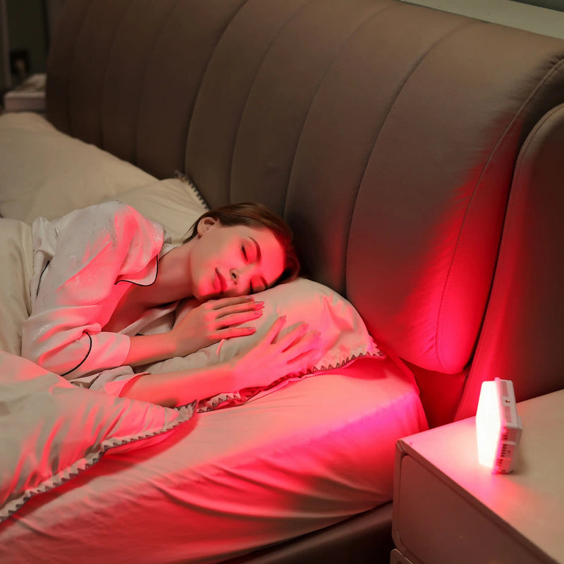 Woman sleeping peacefully in a comfortable bed with a red light therapy device placed on the nightstand emitting a warm glow to aid sleep.