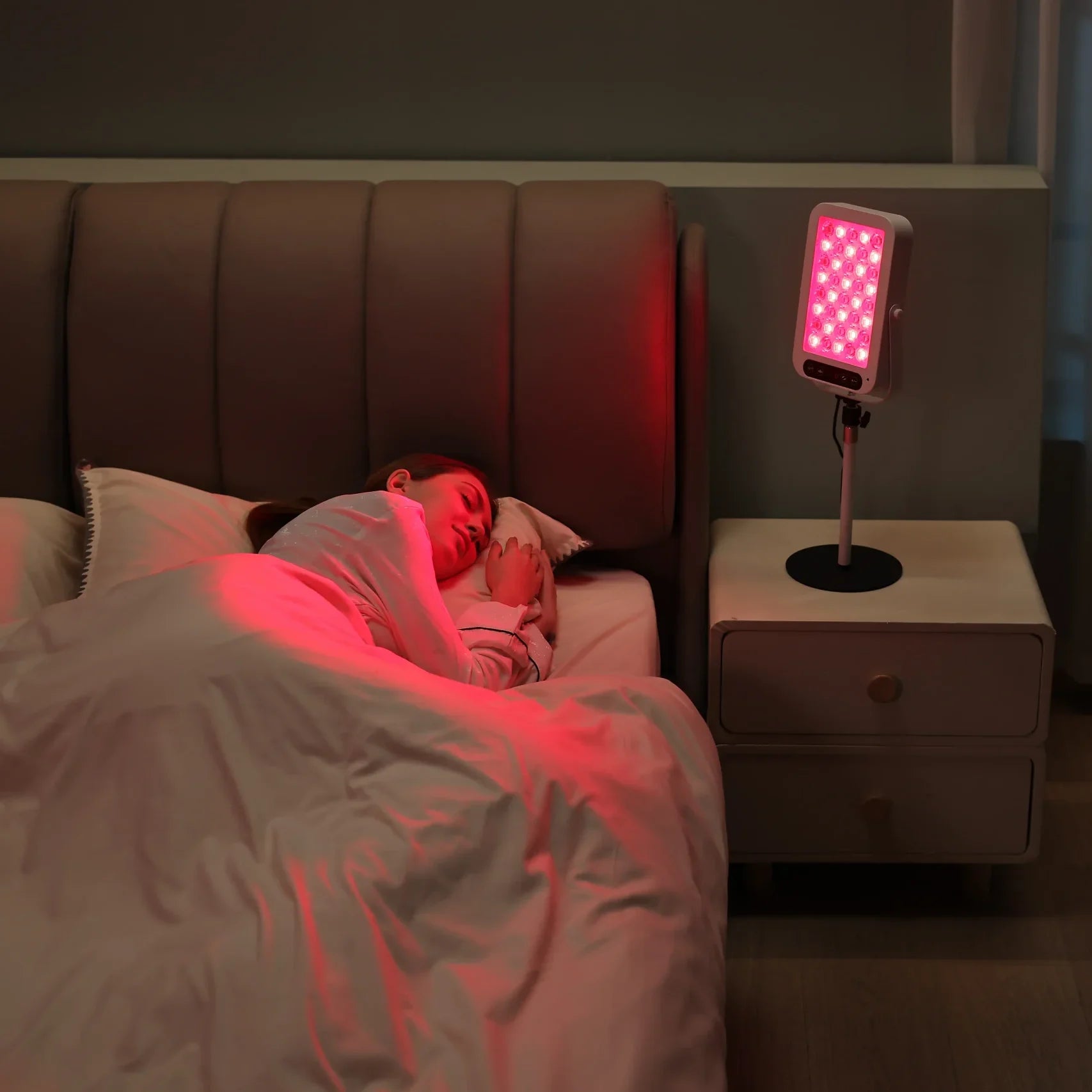Woman sleeping while a YouLumi red light therapy panel glows beside the bed
