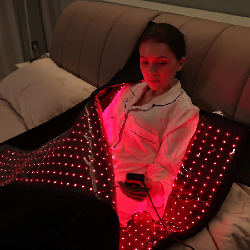 Woman using a red light therapy sleep bag on a bed, holding the remote controller
